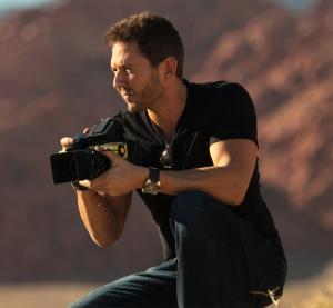 Male Photographer in black clothes kneels in desert with his camera