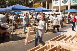 young volunteer carrying a headboard from one station to the next at a well attended bed building event