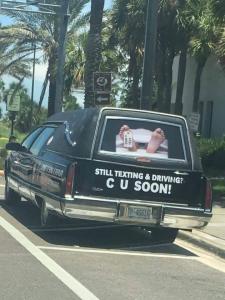 A picture of a hearse, with two feet in the back window. With a message about texting