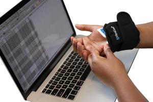 Image of person working at laptop wearing VibraCool Easy Fit on right wrist