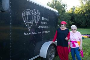 Two women, Louise Vadasz and Elaine Tesler, stand next to a black trailor with "Heaven Bound Ascensions: Hot Air Balloon Team 330-633-3288" written on the side. The women smile and Louise gives a thumbs-up.