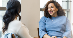 Two women sitting together; one has her back to the camera and the other is facing the camera and smiling
