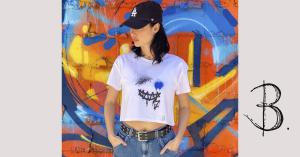 Bridget Bradley, Artist & Designer Models her Exclusive Print Design, Smile Crop Top Tee with Blue Jeans, standing against a colourful city wall with street art