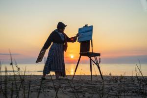 Artist Designer Cynthia Ivey Abitz in silhouette painting the sunrise over Lake Huron.