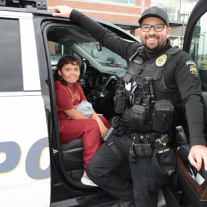 Goodyear police officer smiling as he shows a young girl his police car front seat