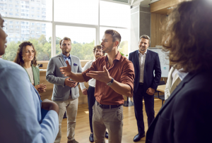 Packetcraft announced wireless mic demo.Man in orange shirt sharing news with people in a circle at a corporate setting.