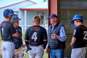 older gentleman in vest giving advice verbally to group of four college boys in jerseys for OK state
