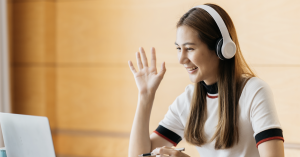 Girl wearing headphones and waving at her laptop.