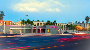 Exterior view of Moxy Phoenix Tempe/ASU hotel at twilight with its distinctive neon sign, palm trees, and a streak of car lights passing by on the road.