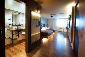 Interior of a Moxy Phoenix Tempe/ASU hotel room showing two beds with a wood-finished floor, an open bathroom vanity with a large mirror, and modern lighting fixtures.