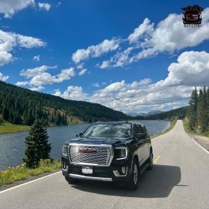 Avo Limo SUV on a 2 lane road in the mountains near vail next to a lake with mountain range in the background