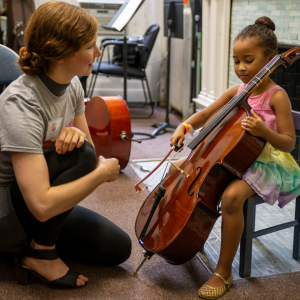 Little girl seated with cello and music teacher