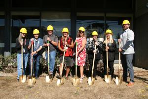 CTCLUSI Tribal Council members and TRHC leadership stand in front of TRHC building in yellow hard hats, holding gold shovels.
