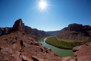 Two hikers walk on a trail on red sandstone overlooking the Green River well below them.