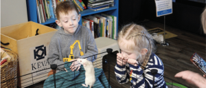 Two kids looking at a white mouse in a cage.