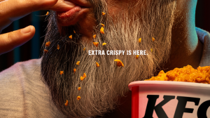 A closeup image of a lengthy silver beard with fried chicken crumbs scattered throughout.  Caption hovering over beard, above KFC bucket says "Extra Crispy is here."