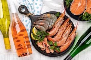 Two pans on a table with various types of seafood next to wine bottles
