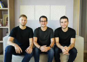Three young men sitting in a living room smiling the the camera