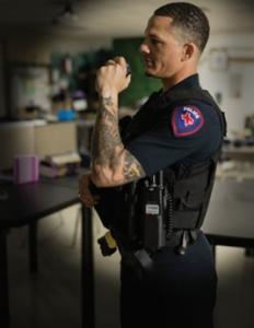 This photograph shows a male police officer talking into the speaker microphone part of a portable radio from Tait Communications.