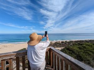 Woman standing on a boardwalk facing the ocean using her phone to see an immersive experience over the Indian Ocean