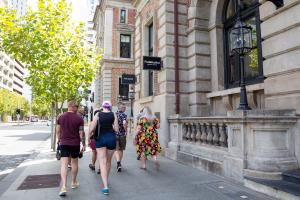 Large group of people walking down St Georges Terrace Perth past a historical building using a walking tour app