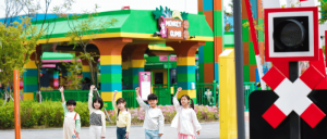 Five Korean children (inside  Legoland Korea Resort) standing and raising their left hands.