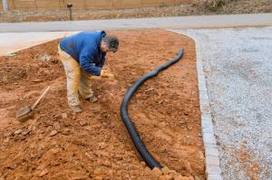 A skilled professional in a blue jacket and khaki attire installs a drainage system to maximize rainwater collection, ensuring adequate water management.