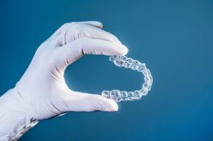 A gloved dentist’s hand delicately holds a clear dental aligner, showcasing its clarity and precision against a serene blue background.