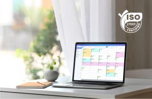 A laptop on a desk displaying Power Diary's calendar feature in a light, airy room, with the ISO 27001 certified logo in the corner.