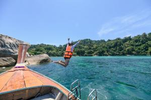 A female tourist wearing a life vest joyfully jumps on a wooden boat amidst the clear blue waters of a tropical sea during a water island adventure tour.