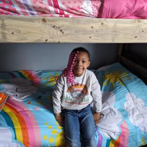 A child sits on the lower bed of a hand-built bunk bed with colorful quilts and bedding.