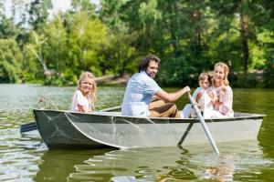 A lovely young family of four is on a rental boat on a calm river surrounded by tall, lush green trees.