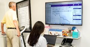 A male patient is standing over a body composition scanner, and Dr. Rotem Amir is analyzing the data on the screen