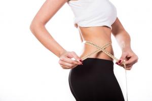 A cropped image of a girl measuring her waist with a tape measure, highlighting the results of body sculpting services on an isolated white background.
