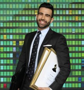 Roy Hage, a Lebanese American opera singer with a modern Arab and Stanford MBA background, smiles confidently in a tailored suit, holding a briefcase and Grammy certificates against a vibrant mosaic backdrop, showcasing his stylish, professional persona.