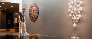  A man stands before a wall, illuminated by a circular light fixture above him, creating a striking visual contrast.