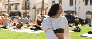 A woman sits on the grass, enjoying the view of a building in the background, surrounded by a serene outdoor setting.