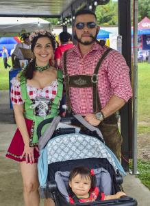 A couple in traditional German Trachten with their child, celebrating at Oktoberfest Miami amidst the vibrant festival atmosphere.