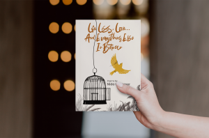 A hand holds a paperback copy of Life, Loss, Love… And Everything Else In Between by Nida Ul Nasser. The cover features a bird flying out of an open cage, symbolizing freedom and healing.
