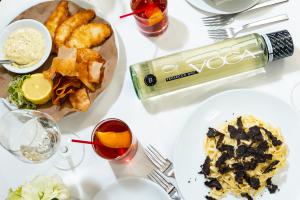 VOGA Prosecco Still bottle on a restaurant table surrounded by dishes such as pasta with black truffles, Italian style fried potatoes and breaded chicken cutlets, and a Still Sbagliato cocktail and