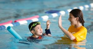 Swim student being high fived by his instructor in the pool.