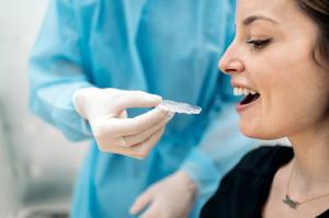 A dentist wearing gloves carefully applies a clear aligner to a delighted female patient's teeth during a treatment session at the clinic.