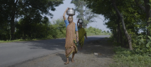 Local women carrying water in buckets on their head, walking on side of road in Nagpur