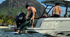 A person loads the SeaNXT Elite underwater scooter onto the back of a Saxdor boat in a scenic tropical location.