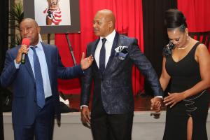 Mayor Sylvester Turner speaks into the microphone with hosts Ferrell Phelps and Sonyia Baring Graham dressed in evening attire.