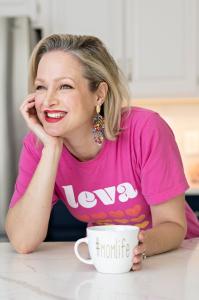 The founder and CEO of Leva, Vanessa Jupe, is pictured here in a kitchen wearing a Leva t-shirt with hearts on it. She has a mug that says #momlife