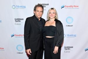 Ben Stiller and daughter Ella stand for photos. Behind them is a wall printed with the Equality Now logo. Ben is wearing a black suit and shirt, Ella is wearing a black crop top, cardigan, and trousers