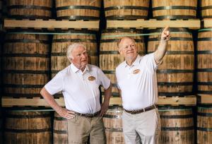 Jackson Purchase Distillery President Lloyd Jones and COO David Salmon pointing into distance inside bourbon warehouse