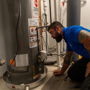 J. Blanton Plumbing technician fixing a residential water heater, highlighting the company’s expertise in water heater installation and repairs for both tank and tankless options.