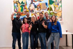 Group photo of the Elevator team smiling and posing with peace signs in front of a colorful art wall, celebrating the expansion to Des Moines.